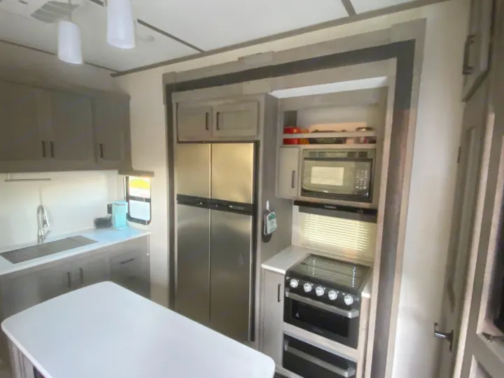 Bright, modern kitchen with stainless steel fridge, oven, microwave, and island in this RV rental, offering full amenities.. Keystone Carbon 2020