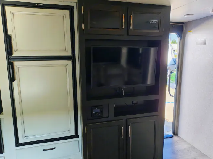 RV rental interior featuring a Dometic refrigerator, Insignia TV entertainment center, and dark wood cabinets.. Jayco JAY FEATHER 26RB 2021