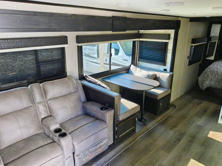 Spacious RV rental interior featuring gray recliners, a dining booth, and a glimpse into the bedroom.. Jayco JAY FEATHER 26RB 2021