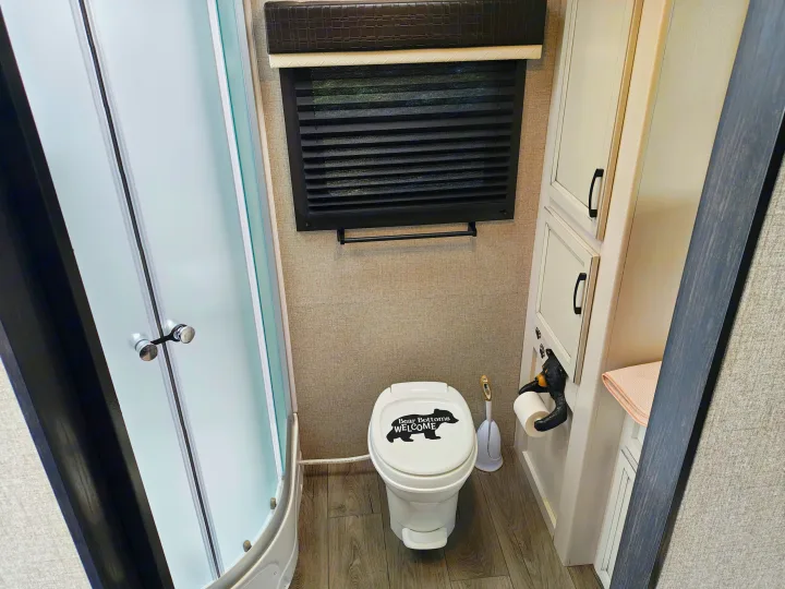 Inside an RV rental, a cozy bathroom features a shower, toilet with a bear decal, and a unique bear-climbing toilet paper holder.. Jayco JAY FEATHER 26RB 2021