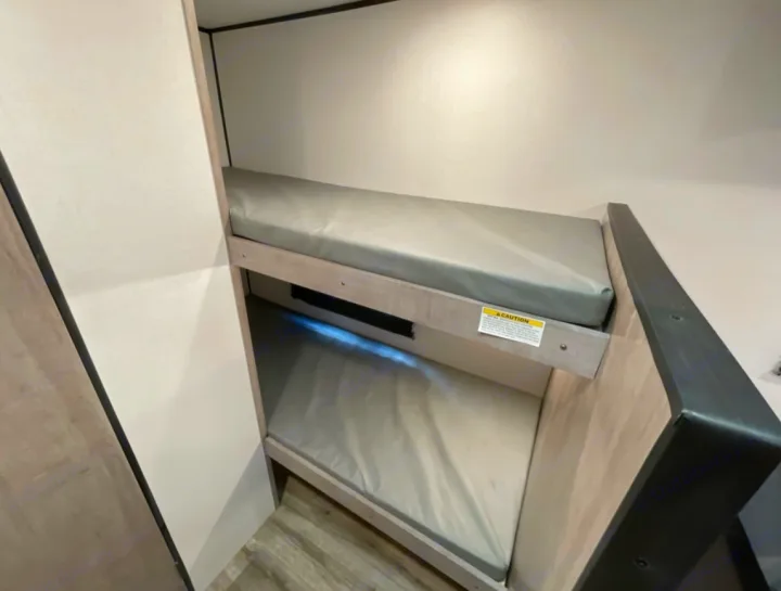 Compact bunk beds with grey mattresses and built-in lighting in an RV rental, ideal for comfortable family travel.. Coleman 17B 2023