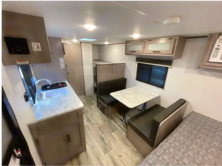 RV rental interior: A modern kitchenette, dinette, bunk beds, and a main sleeping area are visible in this compact RV.. Coleman 17B 2023