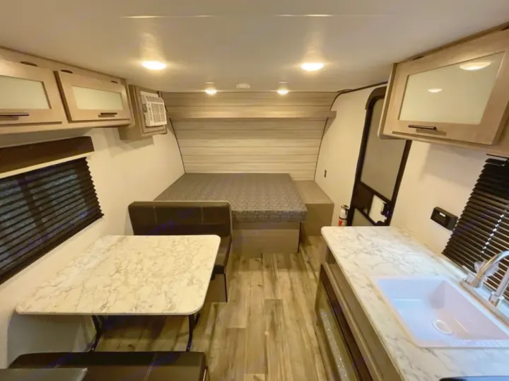 Step inside this RV rental showcasing a comfortable bed, dining table, and compact kitchen area.. Coleman 17B 2023