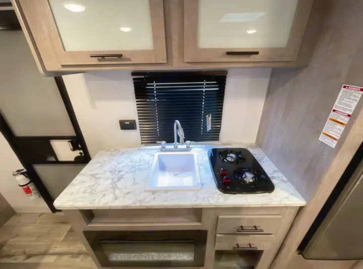 This modern rv rental galley kitchen offers a white sink, two-burner stove, and sleek cabinets. Perfect for cooking on the go.. Coleman 17B 2023