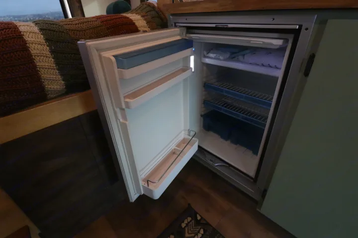 Open compact RV rental fridge, showing wire shelves & freezer. Ready for your road trip essentials.. Chevrolet Express 2011