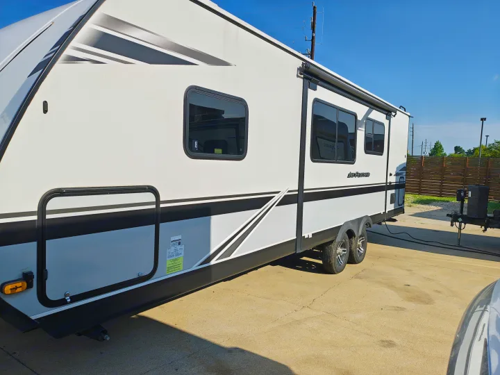 This large white travel trailer, branded 'Jay Feather', is available for rv rental. Note its modern design, black trim, and dual axles.. Jayco JAY FEATHER 26RB 2021