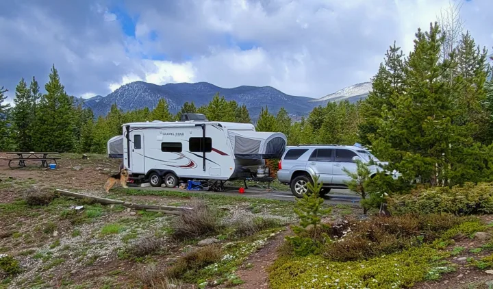 RV rental and SUV at a mountain campsite with a dog and picnic table among pine trees and snow-dusted ground.. Starcraft Travel Star 2014