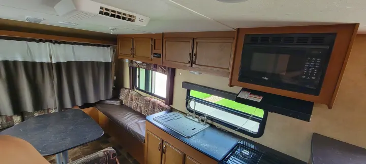 Inside this RV rental: kitchen features a microwave, stove, and sink. Dining area to the left, AC unit overhead.. Starcraft Travel Star 2014