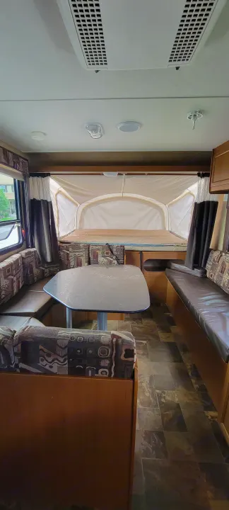 Spacious RV rental interior featuring a comfortable dinette with patterned cushions, a large pop-out bed, AC unit, and tiled floor.. Starcraft Travel Star 2014