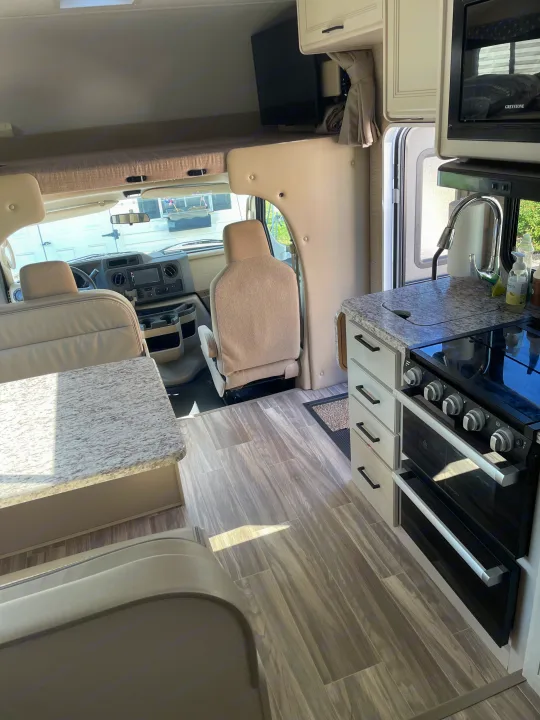Bright rv rental interior, featuring a modern kitchen, dinette, and front cockpit with an overhead bed. Clean, light aesthetic.. Thor Freedom Elite 2022