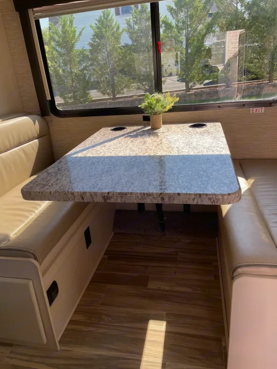 Spacious RV rental dinette featuring a modern speckled table with cup holders & comfortable padded benches for travelers.. Thor Freedom Elite 2022