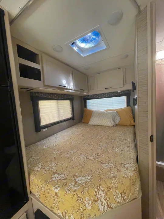 A comfortable RV rental bedroom, featuring a neatly made bed, ample overhead storage, windows, and a ceiling vent.. Thor Freedom Elite 2022