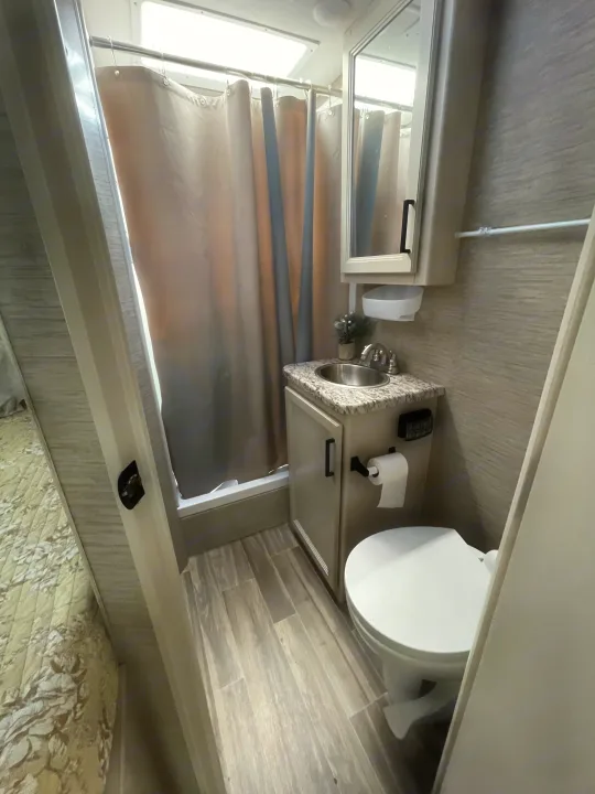 Inside a modern RV rental: compact bathroom with shower, vanity sink, and toilet on wood-look flooring.. Thor Freedom Elite 2022
