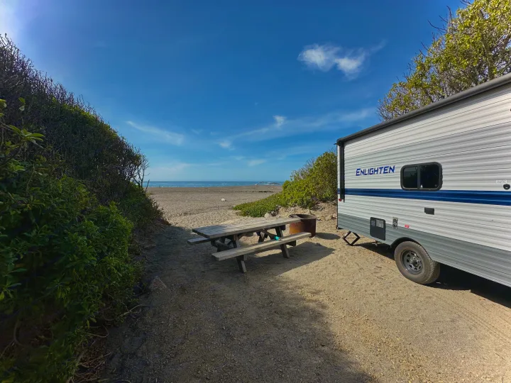 Enlighten RV rental travel trailer at a beachfront campsite with picnic table, fire pit, and ocean views.. Gulf Stream Enlighten 2021