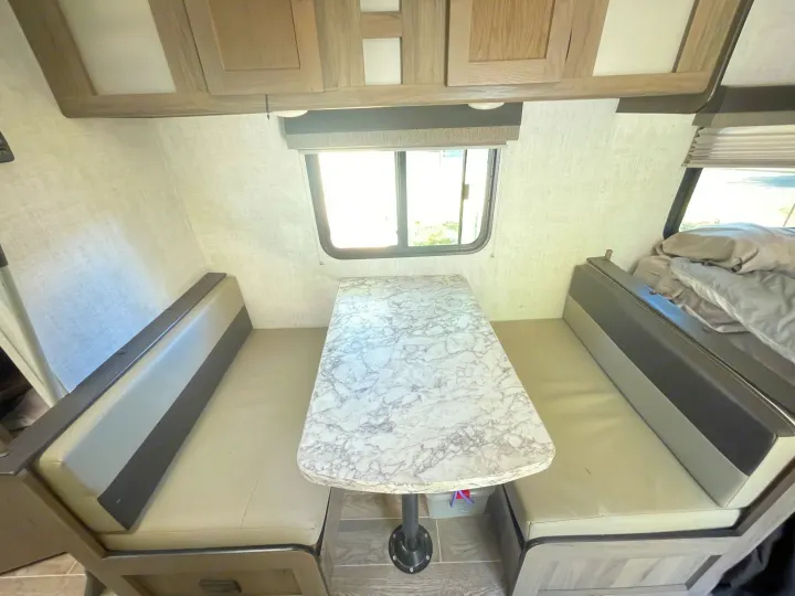 Explore this RV rental's inviting dinette, featuring a marble table, comfy benches, and a nearby bed area.. Gulf Stream Enlighten 2021