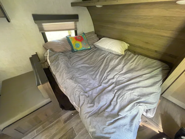 RV rental bedroom: A comfortable bed with pillows, a window with blinds, and light wood interior.. Gulf Stream Enlighten 2021