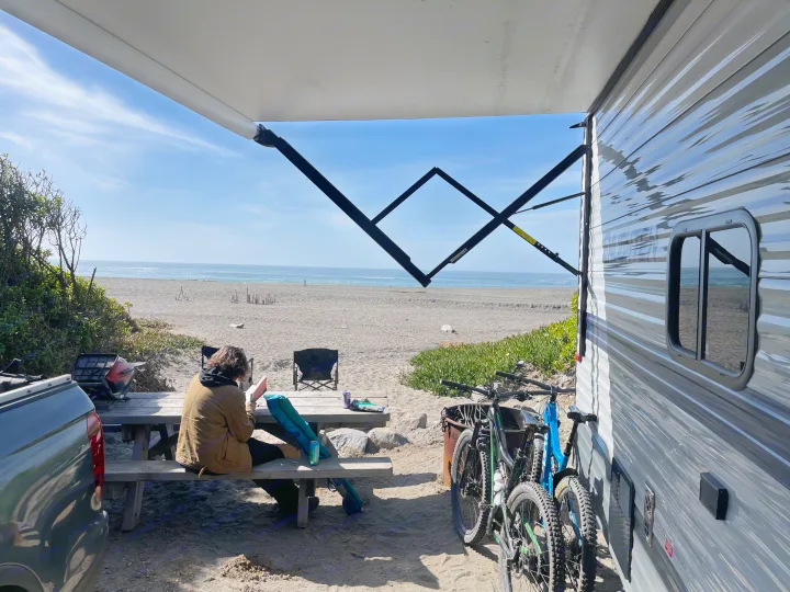 Relaxing at a beachfront RV rental campsite: person reading, ocean views, and bikes ready for adventure.. Gulf Stream Enlighten 2021