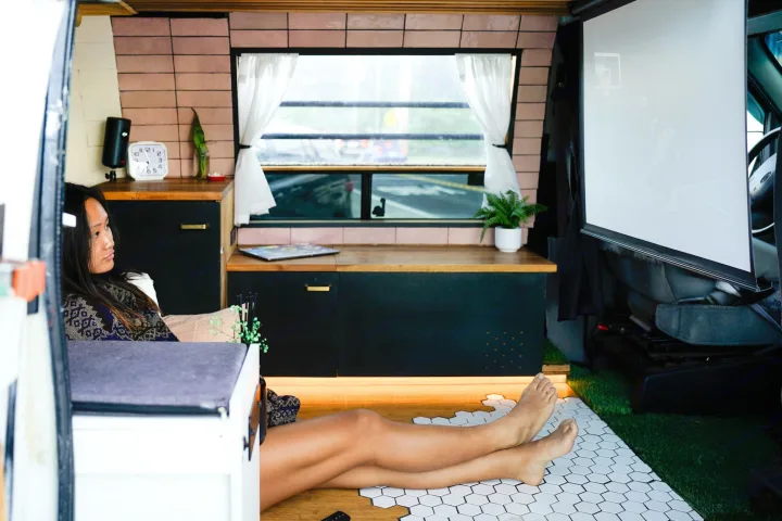 A woman relaxes in a comfortable RV rental, enjoying a game projected on a screen in her custom mobile living space.. Ford Econoline 150 2000
