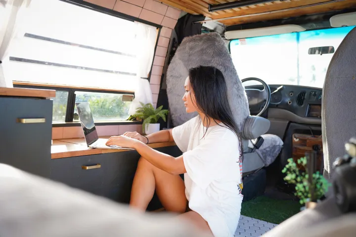 An Asian woman works on her laptop in a bright, modern RV rental. Enjoying mobile remote work and the van life lifestyle.. Ford Econoline 150 2000