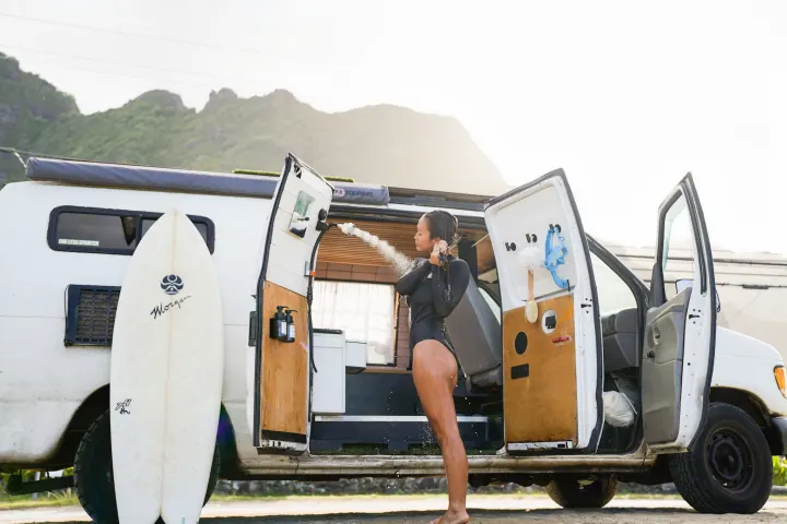 A woman takes an outdoor shower from her custom camper van, a surfboard nearby. Ideal for your next RV rental!. Ford Econoline 150 2000