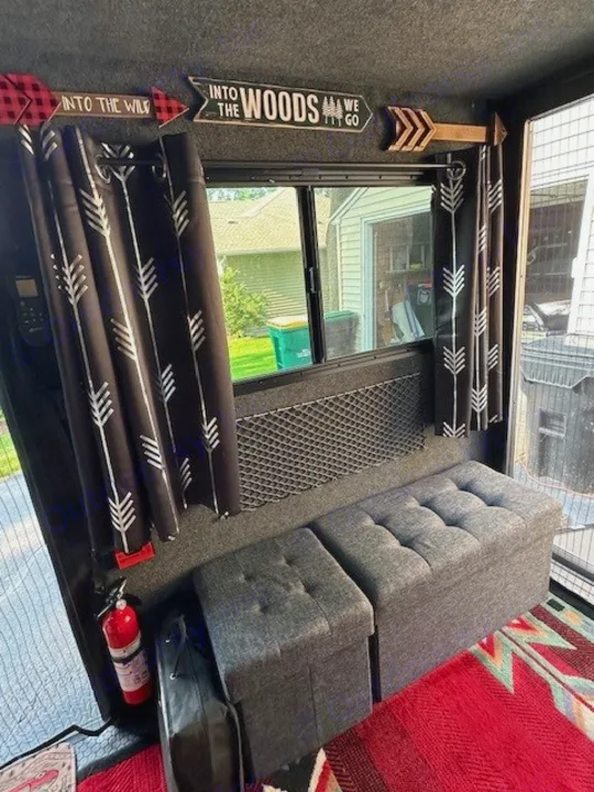 RV rental interior: black arrow curtains, "woods" signs, gray storage benches, and a red fire extinguisher.. Intech Explore 2023