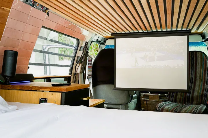 Spacious RV rental interior featuring a comfy bed, pull-down projector screen showing a basketball game, and custom wooden accents.. Ford Econoline 150 2000