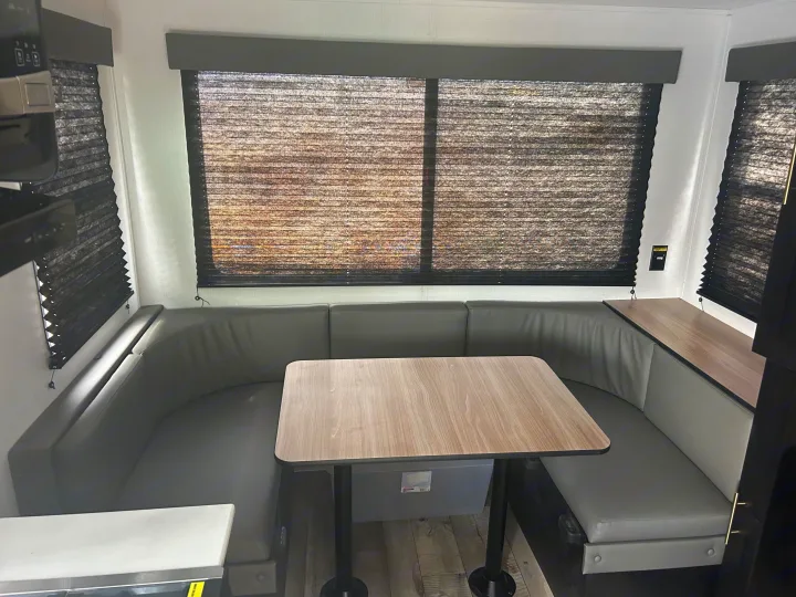 This RV rental features a comfortable U-shaped dinette with gray seating, a wood-grain table, and dark window blinds.. Keystone RV Springdale 2023