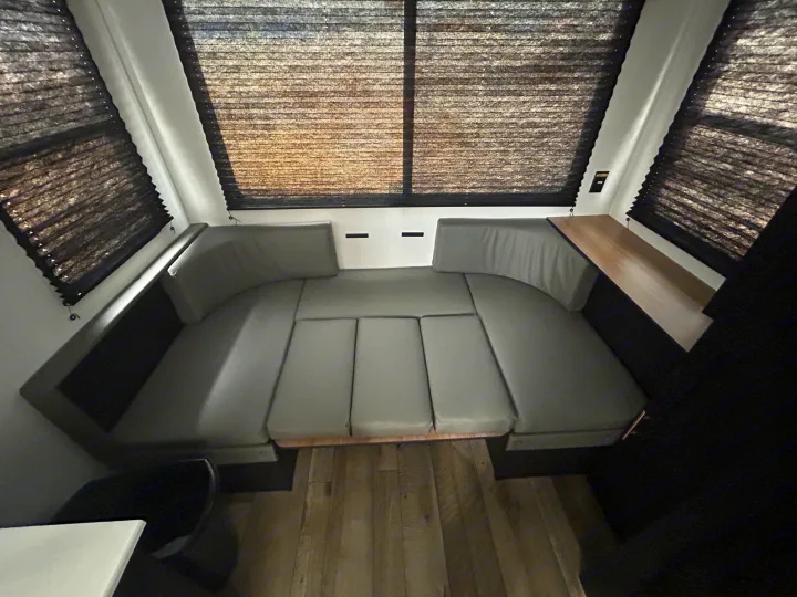 RV rental interior: U-shaped dinette with gray cushions, convertible seating, large windows with pleated blinds, and a small table.. Keystone RV Springdale 2023