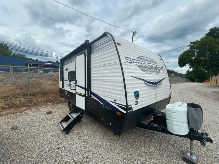 White & black Springdale travel trailer RV rental is parked on gravel, ready for your trip. Steps are extended for easy access.. Keystone RV Springdale 2023