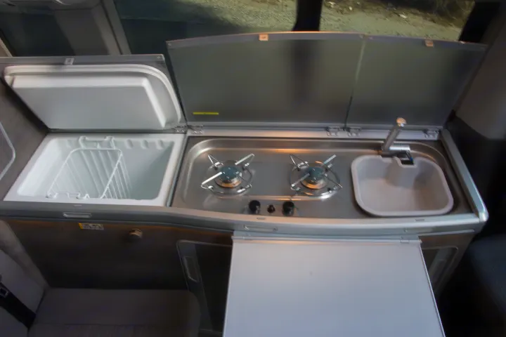RV rental interior: integrated kitchen with refrigerator, twin burners, sink, and an extended table for camping trips.. Volkswagen California Ocean 2025