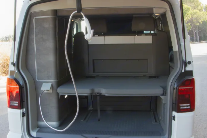 RV rental camper van's modular rear, with pulled-out bed, storage, and outdoor shower hose. Ready for adventures!. Volkswagen California Ocean 2025