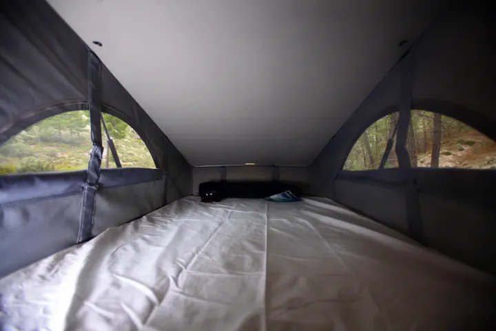 Spacious RV rental pop-top camper interior with a comfortable white bed and scenic forest views outside.. Volkswagen California Ocean 2025