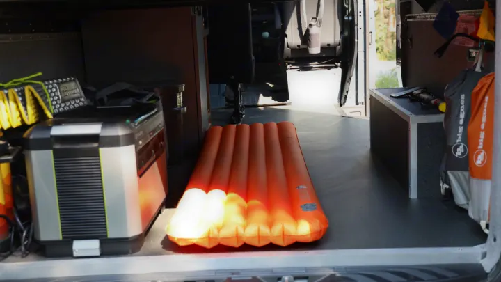 Inside an RV rental van: an orange sleeping pad, portable power, and camping bags, ready for adventure.. Mercedes-Benz Sprinter 2024