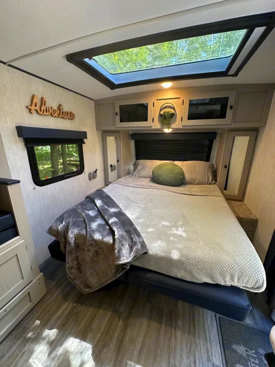 Cozy RV rental bedroom featuring a large bed, overhead cabinets, a skylight, and a window with tree views. Perfect for your adventure.. Coachmen Apex Nano 2024