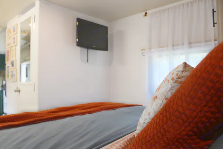 Cozy RV rental bedroom: Features a comfortable bed with orange throw, wall TV, and window with sheer curtains.. Lance Manufacturing Lance Manufacturing Trailer 2015