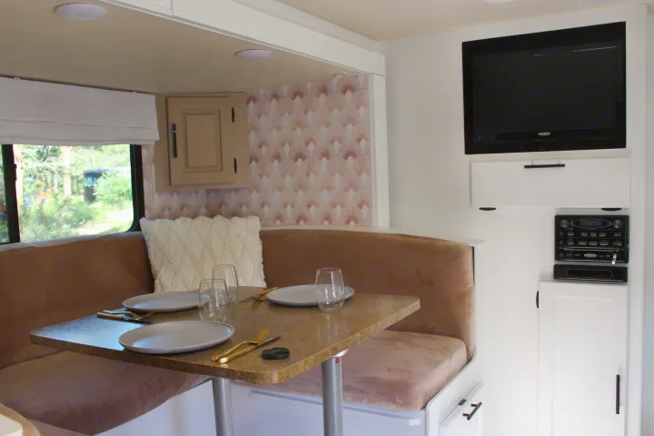 This RV rental's inviting interior features a modern dining booth with a set table, wall-mounted TV, and entertainment system.. Lance Manufacturing Lance Manufacturing Trailer 2015