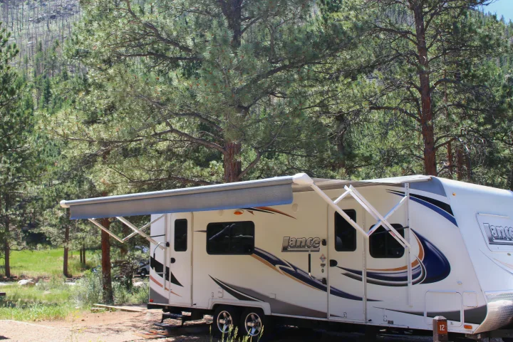 A white RV rental with awning extended at a sunny forest campsite. Explore nature!. Lance Manufacturing Lance Manufacturing Trailer 2015