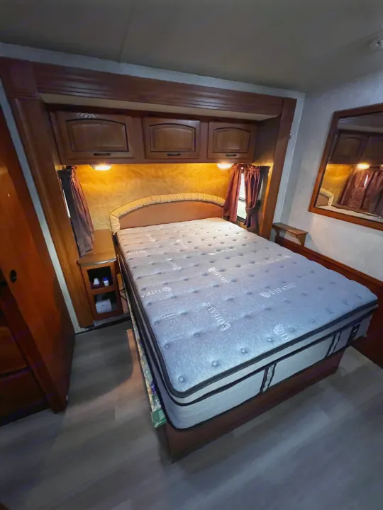 Cozy RV rental bedroom with a large mattress, overhead storage, and a bedside table, illuminated by warm lights.. Forest River Coachmen Mirada 32 DSF 2011