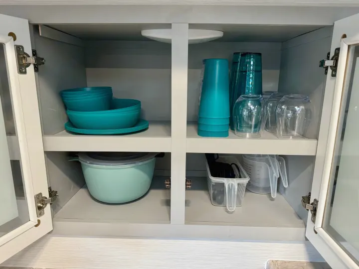 This RV rental kitchen cabinet shows organized teal dishes, cups, and other essentials for a convenient stay.. Forest River Vibe 2021