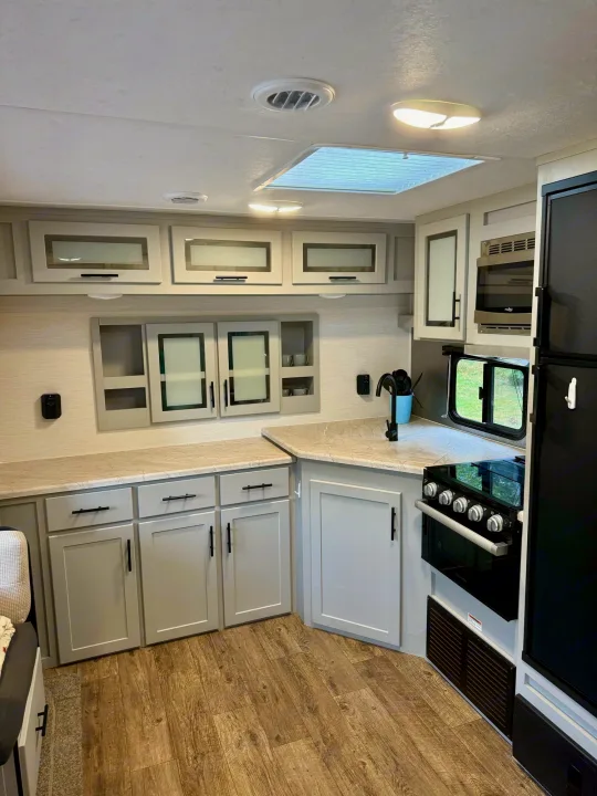 Bright RV rental kitchen with modern gray cabinets, light counters, and essential appliances like stove, microwave, and fridge.. Forest River Vibe 2021