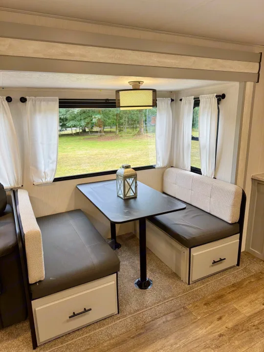 RV rental dinette with two facing benches, central table, under-seat storage, and large window view.. Forest River Vibe 2021