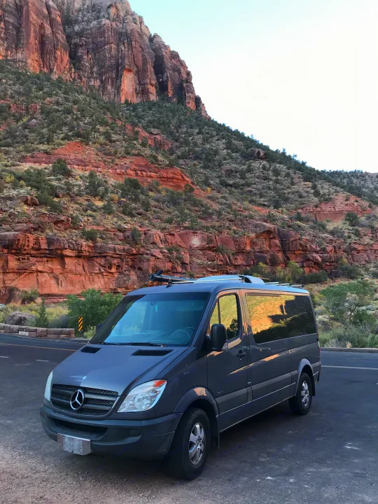 Exploring scenic landscapes with an rv rental: a gray Mercedes Sprinter camper van parked by massive red cliffs.. Mercedes Sprinter 2011