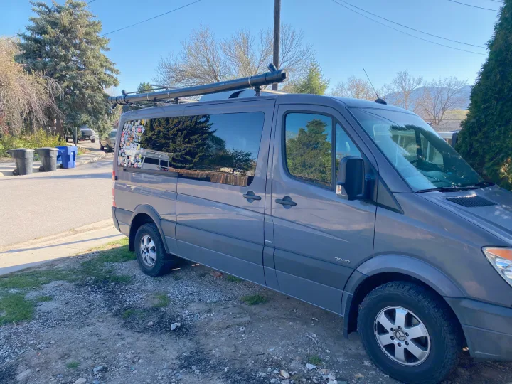 Gray Mercedes Sprinter van, an RV rental, with roof rack and rear window stickers, parked on gravel.. Mercedes Sprinter 2011