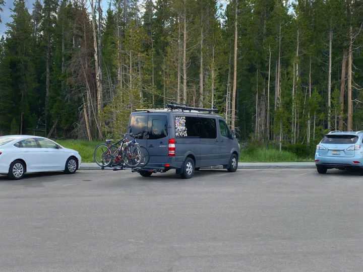 A grey RV rental camper van with bikes parked in a wooded area, ready for outdoor adventures and road trips.. Mercedes Sprinter 2011