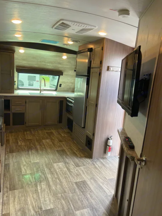 RV rental interior: A bright, modern kitchen with sink, stove, fridge, cabinets, and adjacent living space with TV.. Crossroads sunset trail superlite 2022