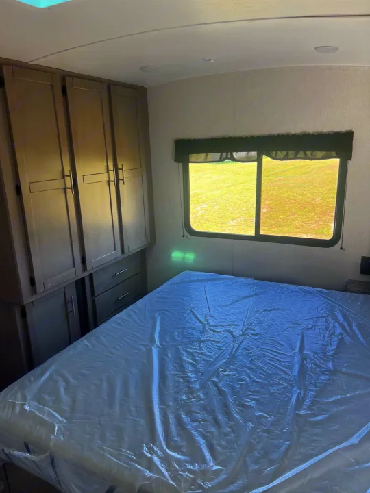 Experience comfort in this RV rental bedroom: bed with protective plastic, built-in storage, and scenic window view.. Crossroads sunset trail superlite 2022