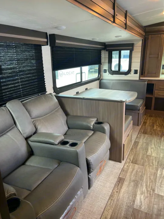 View inside a modern rv rental: gray recliners and dining booth with wood-grain floor.. Crossroads sunset trail superlite 2022