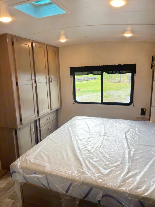 Spacious RV rental bedroom featuring a new bed with protective plastic, built-in storage, and a large window view.. Crossroads sunset trail superlite 2022