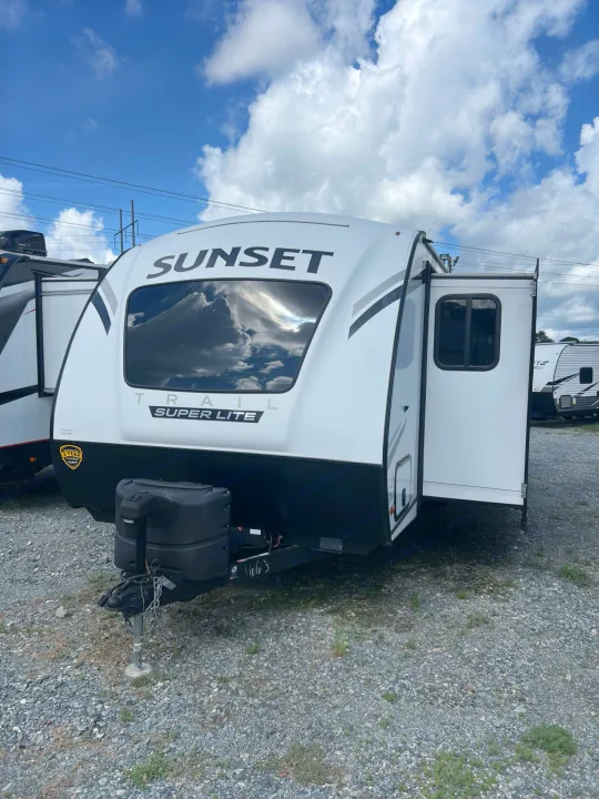 A white Sunset Trail Super Lite RV travel trailer on a gravel lot. Perfect for your next rv rental adventure under a blue, cloudy sky.. Crossroads sunset trail superlite 2022