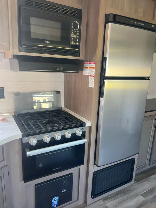 Inside an RV rental, a well-equipped kitchen features a microwave, gas stove with oven, and a tall stainless steel refrigerator.. Starcraft Autumn Ridge 2023